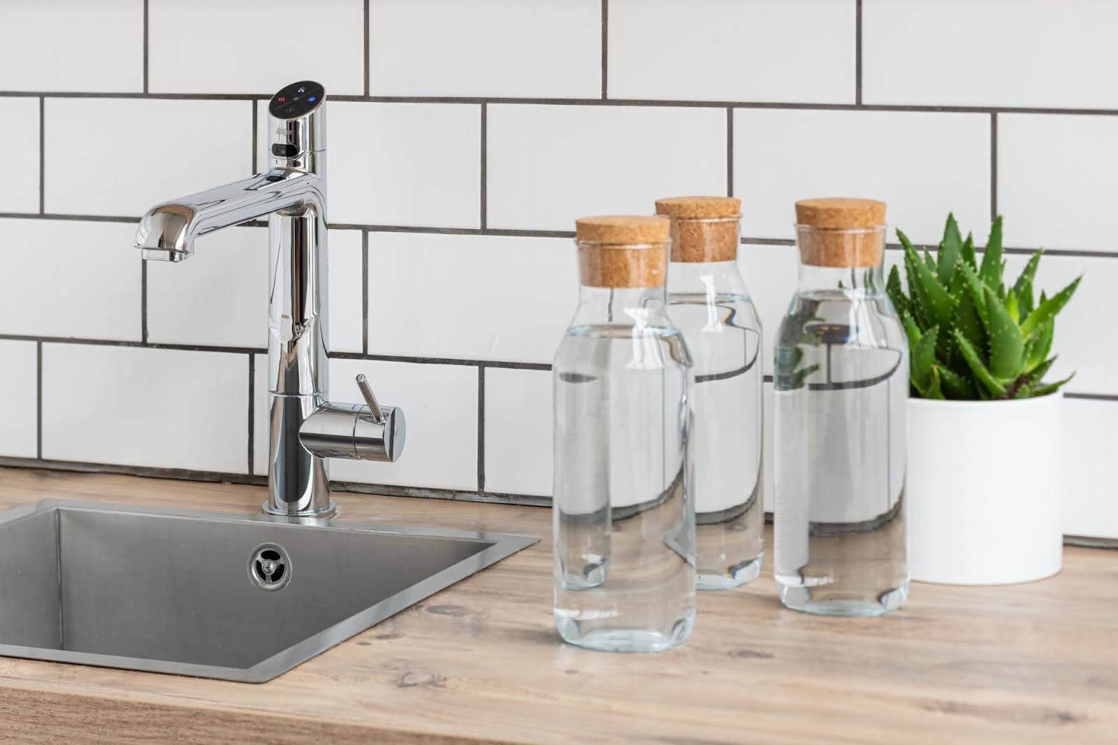 Three glass bottles filled with water and a green plant next to silver HydroTap