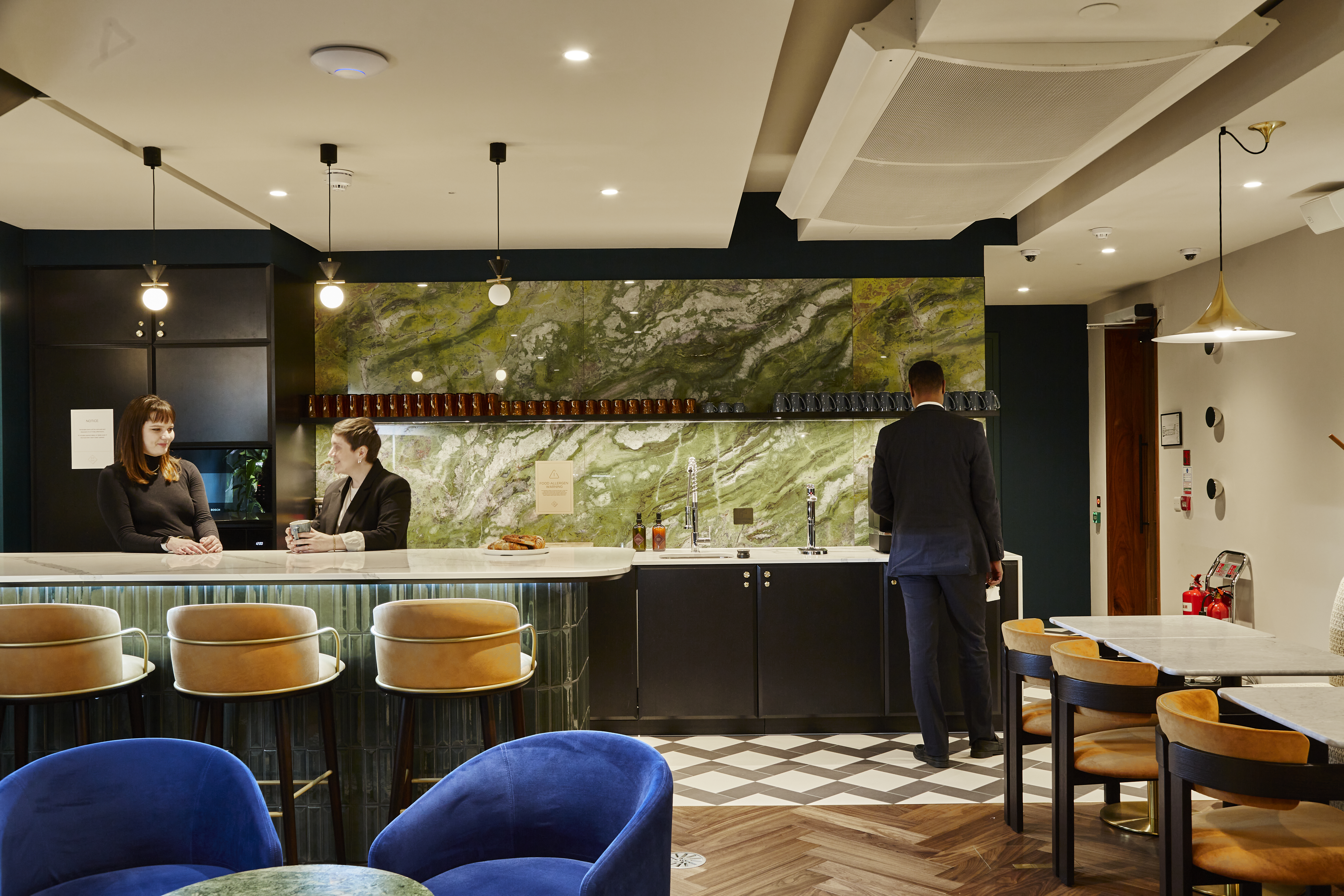 Three employees in a modern office kitchen with green marble and black cabinets.