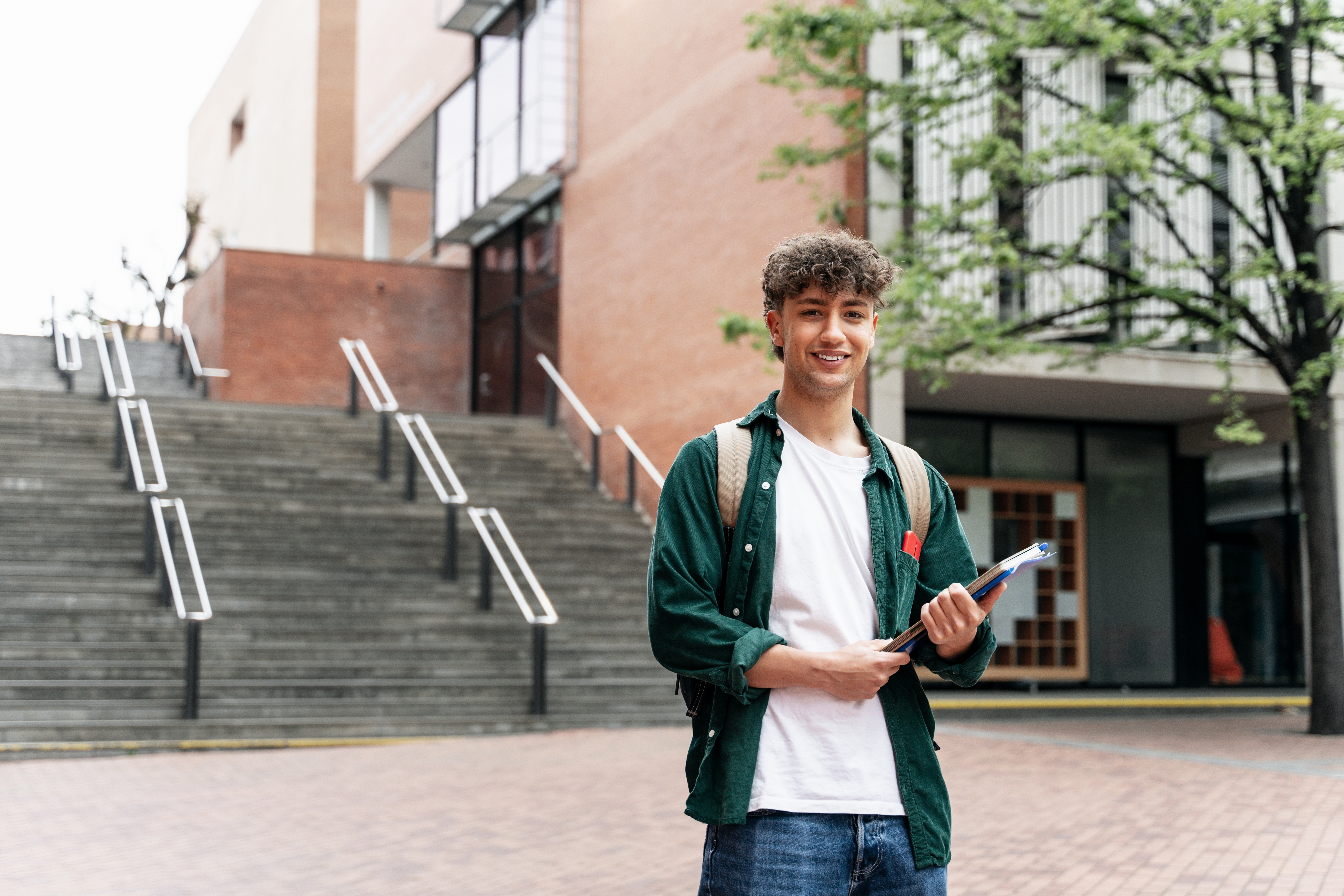 A smiling university student in front of a university building